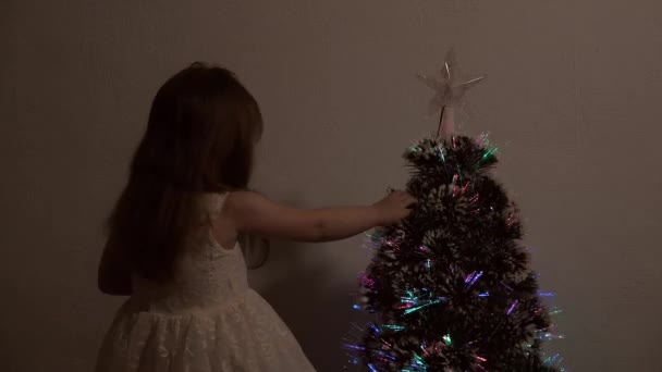 Το χαρούμενο κοριτσάκι παίζει δίπλα στο χριστουγεννιάτικο δέντρο. διακοπές για παιδιά και ενήλικες. Πρωτοχρονιά. Χριστουγεννιάτικο δέντρο, καλές γιορτές. Χριστουγεννιάτικο εσωτερικό. — Αρχείο Βίντεο