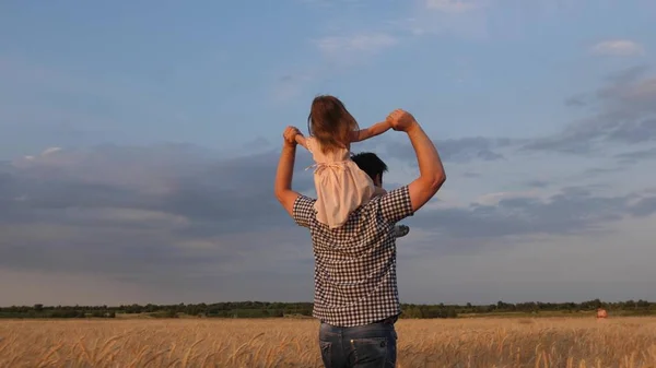 자녀와 부모는 자연스럽게 놀이를 한다. 파란 하늘 과맞선 아버지들의 어깨 위의 행복 한 어린 딸. 아이들 과 아빠는 밀밭을 여행 합니다. 행복 한 가정 과어린 시절의 개념. 느린 동작 — 스톡 사진