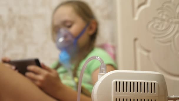 A tablettás gyermek beteg, és inhalátoron keresztül lélegzik. Közelkép. Egy kislány, akit inhalációs maszkkal kezeltek az arcán a kórházban. A kisgyermek az influenzát inhalációs gőz belélegzésével kezeli. — Stock videók