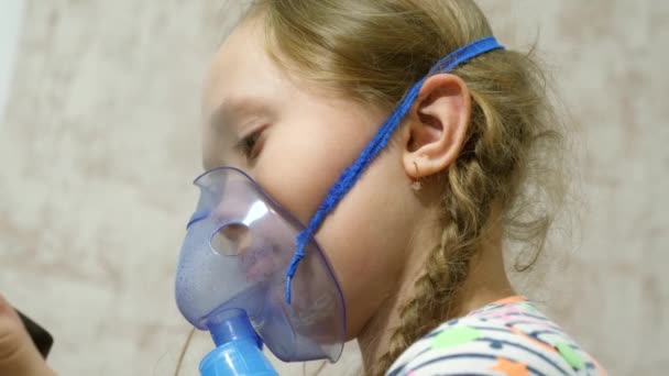 Βήχας θεραπεία. Κοντινό πλάνο. Ένα άρρωστο κορίτσι με μάσκα εισπνέει ένα μπουκάλι σπρέι και παίζει ένα παιχνίδι στον υπολογιστή σε ένα δισκίο. Ένα παιδί με μπλε μάσκα νοσοκομείου εισπνέει αναθυμιάσεις από τους αεραγωγούς στους πνεύμονες.. — Αρχείο Βίντεο