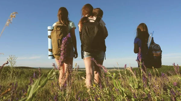 Feliz mamá e hijas, un bebé viajan a través del campo con mochilas en colores en el verano. Vida familiar. Las chicas turísticas y un bebé acampan en el bosque. Viajeros del trabajo en equipo — Foto de Stock