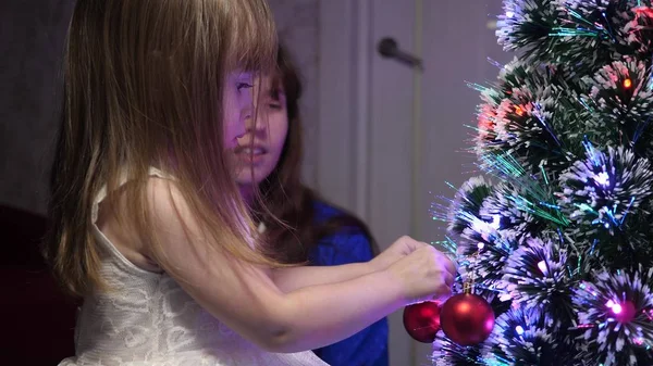 아기 엄마는 크리스마스 트리에 빨간 공 장난감을 걸어 놓고. 행복 한 어린 시절의 컨셉. 아이와 엄마는 크리스마스 구슬로 나무를 장식합니다. 어린 아이와 부모님 이 크리스마스 트리에서 연주를 하고 있습니다. — 스톡 사진