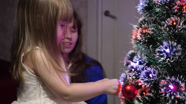 Bébé et maman accrochent un jouet boule rouge sur l'arbre de Noël. concept d'enfance heureuse. enfant et mère décorer arbre avec des boules de Noël. petit enfant et un parent jouent près de l'arbre de Noël . — Photo