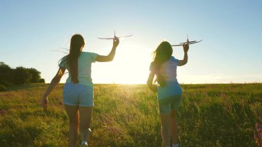 Mutlu çocukluk kavramı. Uçma hayalleri. Gün batımında iki kız bir oyuncak uçakla oynuyor. Güneşin arka planındaki çocuklar ellerinde bir uçakla. Uçakta oynayan çocukların silueti