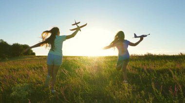 Mutlu çocukluk kavramı. Uçma hayalleri. Gün batımında iki kız bir oyuncak uçakla oynuyor. Güneşin arka planındaki çocuklar ellerinde bir uçakla. Uçakta oynayan çocukların silueti