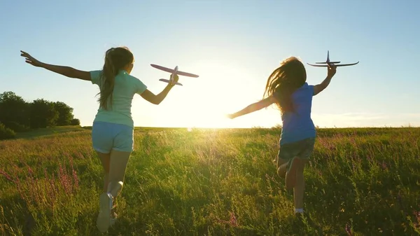 Szczęśliwego dzieciństwa. Marzenie o lataniu. Dwie dziewczyny bawią się zabawkowym samolotem o zachodzie słońca. Dzieci na tle słońca z samolotem w ręku. Sylwetka dzieci bawiących się w samolocie — Zdjęcie stockowe
