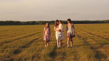 Çocuklar ve anne çayırda oynuyorlar. Mutlu aile kavramı. Parkta yürüyen kız kardeşleri olan bir anne ve küçük kız. Bir yaz tarlasında yürüyen çocuklu mutlu bir aile..