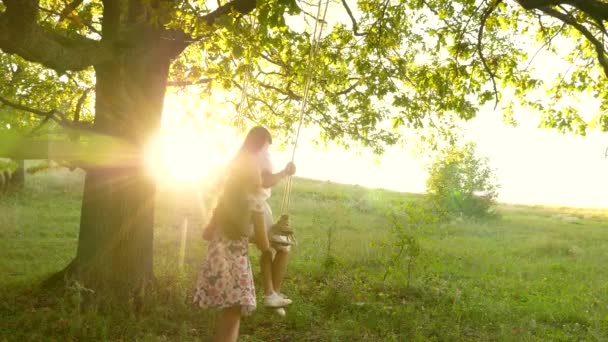Children swinging on swing on an oak branch in sun. Dreams of flying. concept of happy childhood. Beautiful girls are playing in park. teenage girls enjoy flying on swing on a summer evening in forest — Stock Video