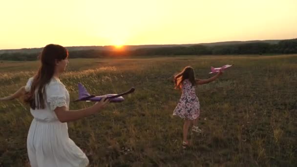 Bambini nel prato con un aeroplano in mano. Sogni di volare. Il concetto di un'infanzia felice. Due ragazze giocano con un aeroplano giocattolo sul campo. Silhouette di bambini che giocano su un aereo . — Video Stock