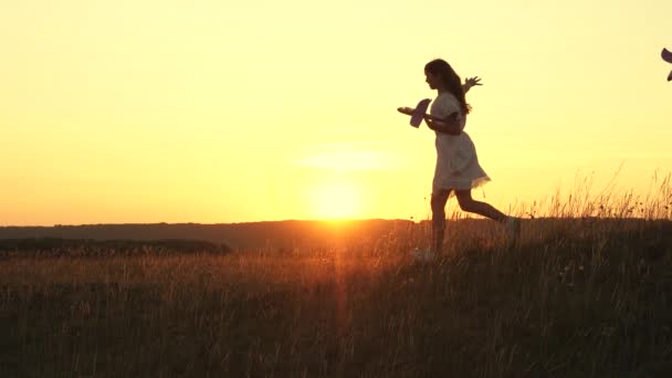 Avion jouet dans les mains des filles qu'ils jouent sur le terrain. heureux enfants dans une prairie avec un avion à la main. Rêves de vol. concept d'une enfance heureuse. Silhouette d'enfants jouant dans un avion . — Video