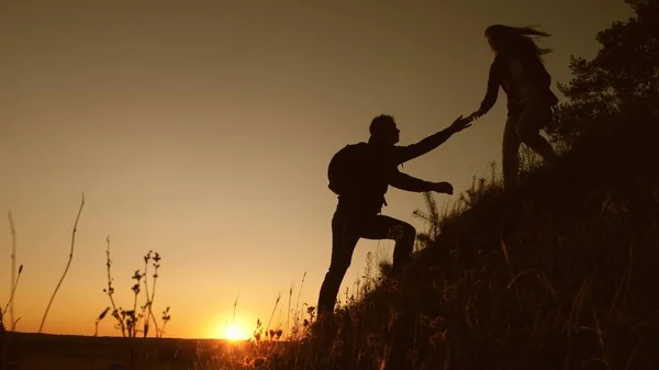 Travelers descend from mountain at sunset, hold hands. adventure and travel concept. teamwork of business people. Hiker man holds out his hand to a woman traveler descending from top of hill. — Stock Photo, Image