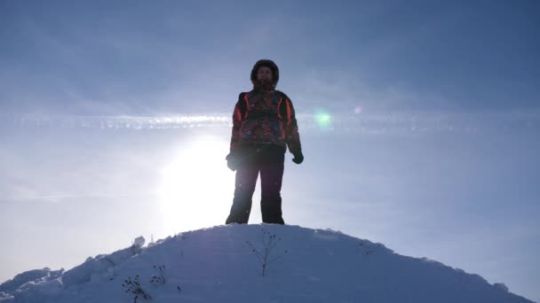 Viajante sobe um pico de montanha. O viajante do Alasca vai ao topo de uma colina nevada e alegra-se na vitória contra um pôr-do-sol de inverno. Mountaineer Viagem às montanhas no inverno. Alpinista viaja caminhadas . — Vídeo de Stock