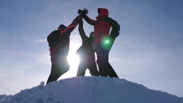travelers met on top of success. Tourists come to top of snowy hill and rejoice at victory against backdrop of a yellow sunset. teamwork and victory. team work of people in difficult conditions