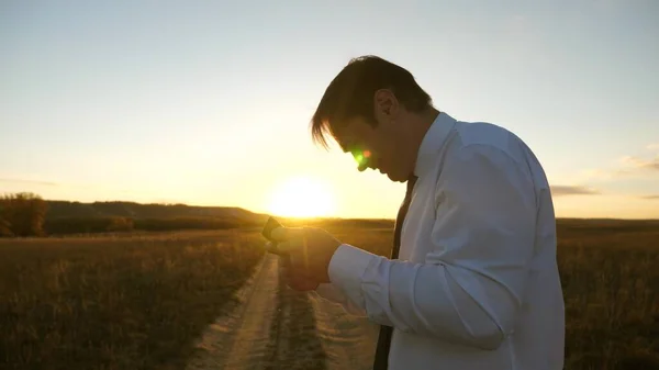 Homem de negócios jogando jogos de tablet no parque nos raios quentes do pôr do sol. homem jogando jogos no smartphone. homem feliz na camisa branca e empate joga online no tablet . — Fotografia de Stock