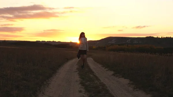 Sexy Business woman walking along a country road with a briefcase in hand, the sun shimmers at sunset. Sexy business girl working in the countryside. beautiful girl travels the countryside. — Stock Photo, Image