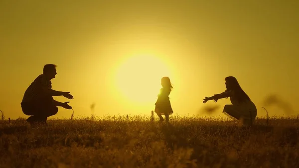 Bebé feliz va de papá a mamá. padres se les enseña a caminar a un niño pequeño, niña hace sus primeros pasos en el sol, cámara lenta. padres juegan con su hijita . — Foto de Stock