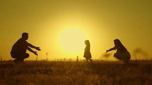 Bebé feliz va de papá a mamá. padres se les enseña a caminar a un niño pequeño, niña hace sus primeros pasos en el sol, cámara lenta. padres juegan con su hijita . — Foto de Stock