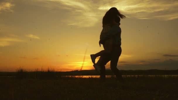 Pareja joven bailando al atardecer en la playa. Feliz chico y chica vals en la noche en el parque de verano. Amor hombre y mujer bailan en brillantes rayos de sol en el fondo del lago . — Vídeo de stock