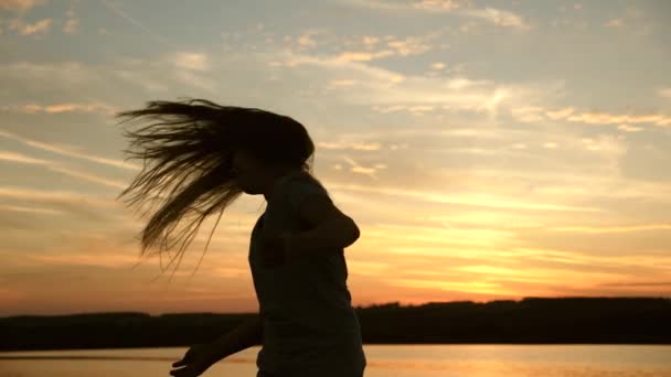 Dívka tančí při západu slunce s dlouhými vlasy v paprscích západu slunce. žena se rozsvítí na plese na pláži. Večerní večírek u moře. Zpomalený pohyb — Stock video