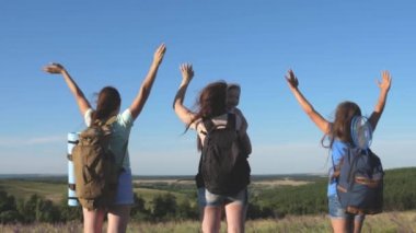Gezgin kadınlar ellerini kaldırır ve sevinirler. Anne ve çocuklar turisttir. Takım çalışması gezginleri. macera konsepti. Bir grup turist bir çiçek tarlasından geçer ve dağdan doğanın tadını çıkarırlar..