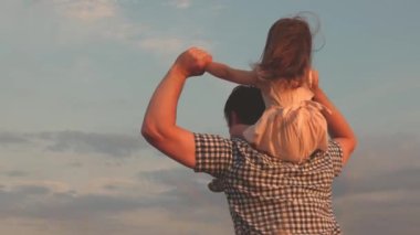 Çocuk ve ebeveyn doğada oynarlar. Mavi gökyüzüne karşı tarlada babasının omuzlarında küçük mutlu bir kız. Bebek ve babası buğday tarlasında seyahat ediyorlar. Mutlu aile ve çocukluk kavramı. Yavaş çekim