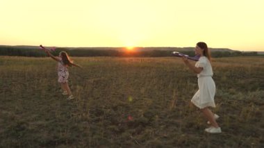 Ellerinde bir uçakla çayırdaki çocuklar. Uçma hayalleri. Mutlu bir çocukluk kavramı. İki kız sahada oyuncak bir uçakla oynar. Uçakta oynayan çocukların silueti.