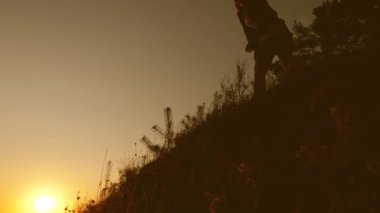 macera ve seyahat konsepti. Kadın gezgin, tepenin zirvesine tırmanan bir adama elini uzatır. Turistler gün batımında el ele tutuşarak dağa tırmanırlar. iş adamlarının takım çalışması
