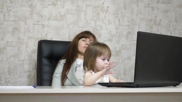 Yorgun anne, küçük kızı ile birlikte ofiste bilgisayar başında çalışıyor. İş kadını kucağında bebekle dizüstü bilgisayarda çalışıyor. Serbest çalışan bir kadın işi. Modern annelik — Stok fotoğraf