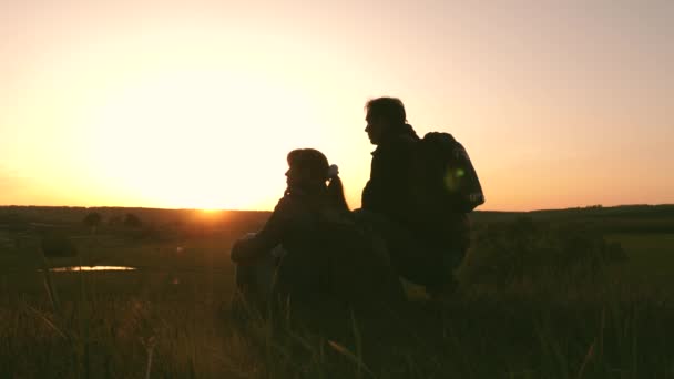 Toeristen met rugzakken man en vrouw en kijken naar de zonsondergang. vrije reizigers rusten op een heuveltop en genieten van zonsondergang. silhouet van reiziger, zittend op heuveltop. begrip vrijheid, dromen en avonturen — Stockvideo