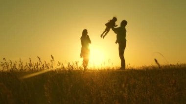 Çocuk, baba ve anne güneşte çayırda oynuyorlar. Mutlu çocukluk kavramı. Anne, baba ve küçük kız güneşin altında bir tarlada yürüyorlar. Mutlu, genç bir aile. Mutlu aile kavramı.