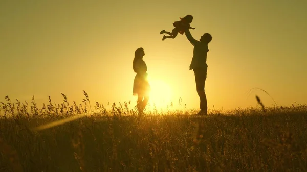 太陽の下でお父さんもお母さんも草原で遊んでいます幸せな子供時代の概念です母と父と娘は太陽の下で畑を歩いていました幸せな若い家族だ幸せな家族という概念は. — ストック写真