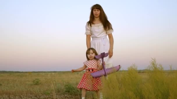 Niño con un juguete juega con su madre en el prado. niño sostiene un avión de juguete en sus manos. familia feliz camina por la noche fuera de la ciudad. hija y madre caminan por el campo . — Vídeos de Stock