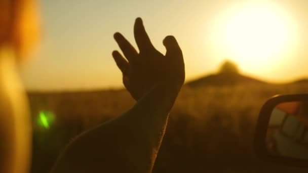 Ein Mann, der aus dem Autofenster kommt, spielt mit den Fingern mit Sonnenstrahlen. Die Hand des Fahrers spielt mit der Sonne aus dem Autofenster gegen den schönen Sonnenuntergang. Mädchenhand winkt die Sonne. Anreise mit dem Auto — Stockvideo