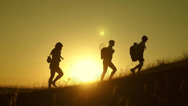 Children and mom with backpacks travel climb mountain in the sun. mom and daughters go camping. Family of tourists with kids traveling at sunset. joint work of tourists. movement to victory. — Stock Photo, Image