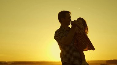 Babası kucağındaki sevgili çocuğu uçarken dans eder ve güler. Mutlu bebek gün batımında babasıyla oynuyor. Bir adam ve bir çocuğun silueti. Aile kavramı