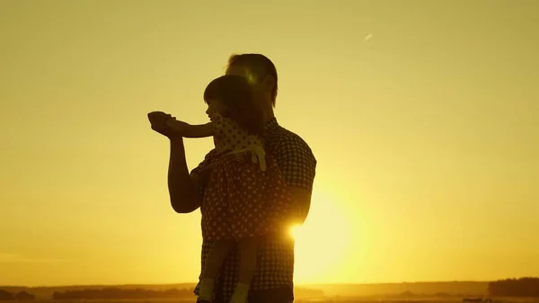 Vader geliefde kind in haar armen danst tijdens de vlucht en lacht. Gelukkige baby speelt met zijn vader bij zonsondergang. Silhouet van een man en een kind. Gezinsconcept — Stockfoto