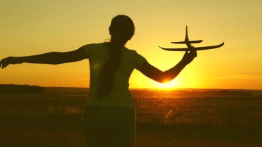 çocuklar oyuncak uçak oynarlar. Mutlu kız gün batımı ışığında bir alanda bir oyuncak uçak ile çalışır. uçan ve pilot olma genç hayalleri. kız bir pilot ve astronot olmak istiyor.