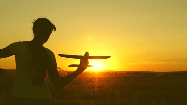 Barn leker leksaksflygplan. Happy Girl körs med en leksak flygplan på ett fält i solnedgången ljus. tonåring drömmer om att flyga och bli pilot. flickan vill bli pilot och astronaut. — Stockfoto