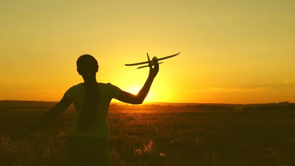 Niños juegan juguete avión. Chica feliz corre con un avión de juguete en un campo en la luz del atardecer. adolescente sueña con volar y convertirse en piloto. la chica quiere convertirse en piloto y astronauta . — Foto de Stock