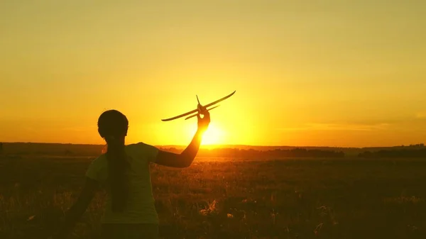 children play toy airplane. Happy girl runs with a toy airplane on a field in the sunset light. teenager dreams of flying and becoming pilot. the girl wants to become a pilot and astronaut.