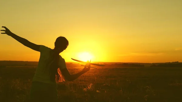 Niños juegan juguete avión. Chica feliz corre con un avión de juguete en un campo en la luz del atardecer. adolescente sueña con volar y convertirse en piloto. la chica quiere convertirse en piloto y astronauta . —  Fotos de Stock