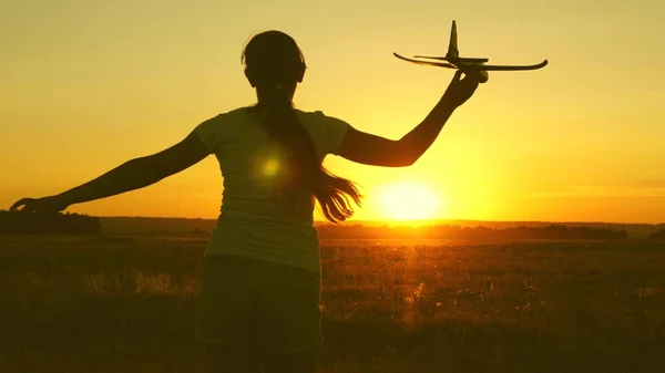 As crianças brincam de avião de brinquedo. Menina feliz corre com um avião de brinquedo em um campo sob a luz do pôr do sol. sonho adolescente de voar e se tornar piloto. a menina quer se tornar um piloto e astronauta . — Fotografia de Stock