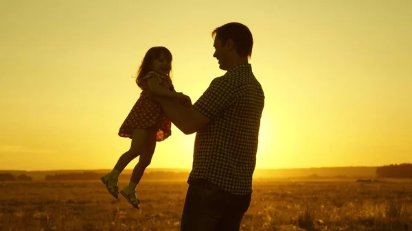 Tata ukochany dziecko w jej ramionach tańczy w locie i śmieje się. Szczęśliwe dziecko bawi się z ojcem o zachodzie słońca. Sylwetka mężczyzny i dziecka. Koncepcja rodziny — Zdjęcie stockowe