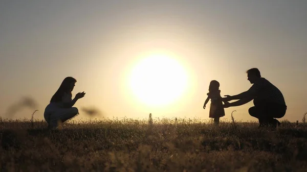 Rodiče si hrají se svou malou dcerou. matka a tatínek si hrají se svou dcerou na slunci. šťastné dítě chodí od táty k mámě. mladá rodina v terénu s dítětem 1 rok. koncepce rodinných štěstí. — Stock fotografie