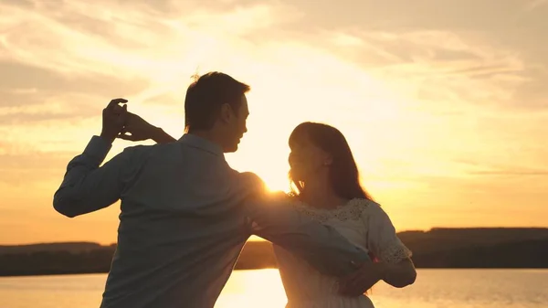 Sevgi dolu erkek ve kadın gölün arka planda güneşin parlak ışınları dans. Genç çift sahilde gün batımında dans ediyor. Yaz parkında akşam mutlu adam ve kız vals.