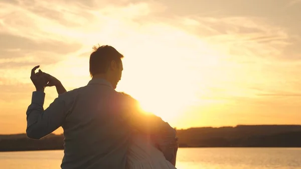 Amare l'uomo e la donna danzano in raggi di sole sullo sfondo del lago. Giovane coppia che balla al tramonto sulla spiaggia. Felice ragazzo e ragazza valzer la sera nel parco estivo . — Foto Stock