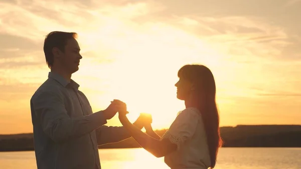 Milující muž a žena tančí v jasných slunečních paprscích na pozadí jezera. Mladí manželé tančí při západu slunce na pláži. Šťastný muž a dívka valčík večer v letním parku. — Stock fotografie