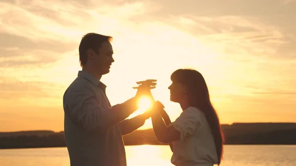 Loving man and woman dance in bright rays of sun on the background of the lake. Young couple dancing at sunset on beach. Happy guy and girl waltz in the evening in the summer park.