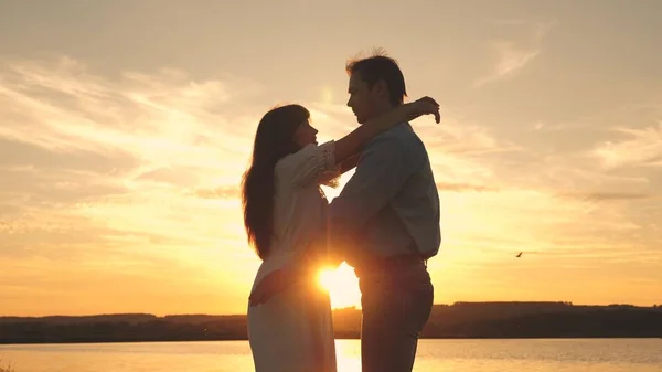 Milující muž a žena tančí v jasných slunečních paprscích na pozadí jezera. při západu slunce na pláži. Šťastný chlap a dívka valčík ve večerních hodinách v letním parku. — Stock fotografie