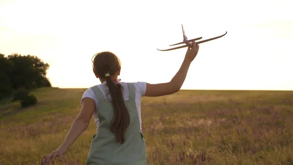 Giovane ragazza corre con un aereo giocattolo sul campo nei raggi di slint. i bambini giocano aereo giocattolo. adolescente sogna di volare e diventare un pilota. la ragazza vuole diventare un pilota e astronauta . — Foto Stock